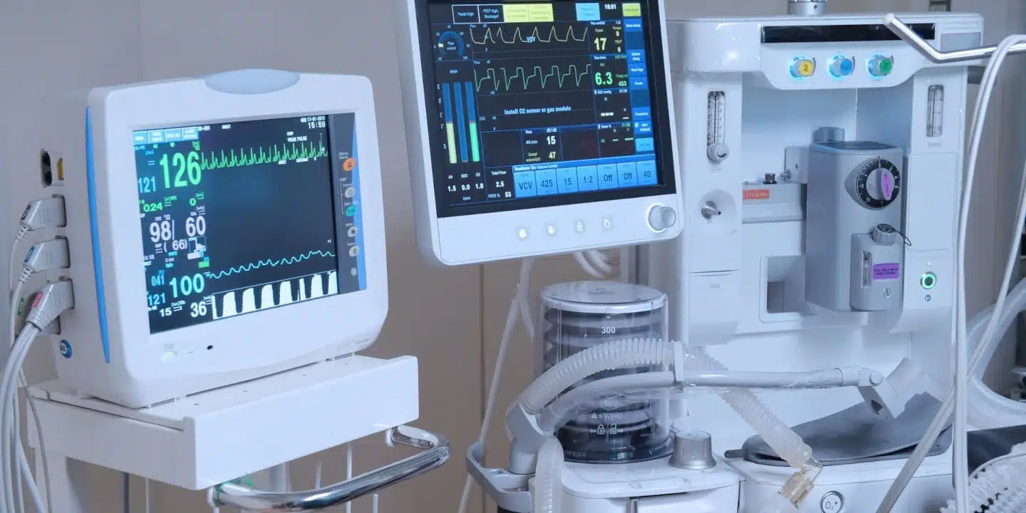 Medical monitors and equipment display vital signs and respiratory data in a hospital room.