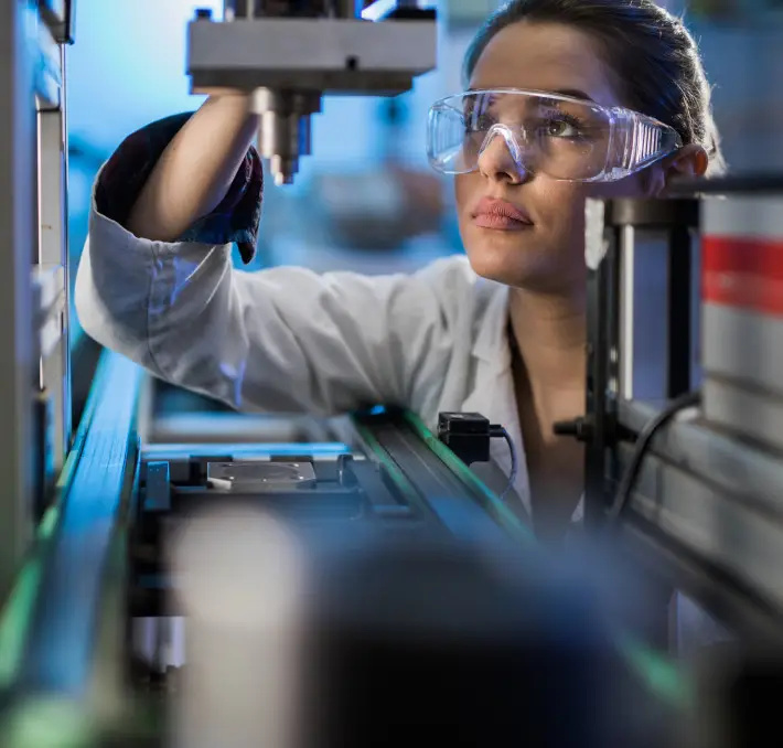 A person wearing safety goggles and a lab coat operates scientific equipment in a laboratory setting.