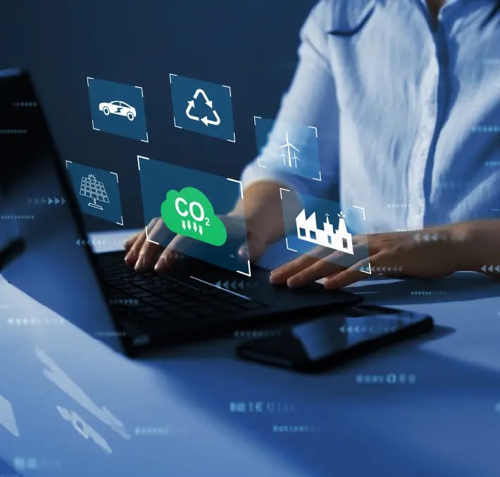Person typing on a laptop with virtual icons representing carbon emissions, renewable energy, recycling, and environmental sustainability displayed above the keyboard.