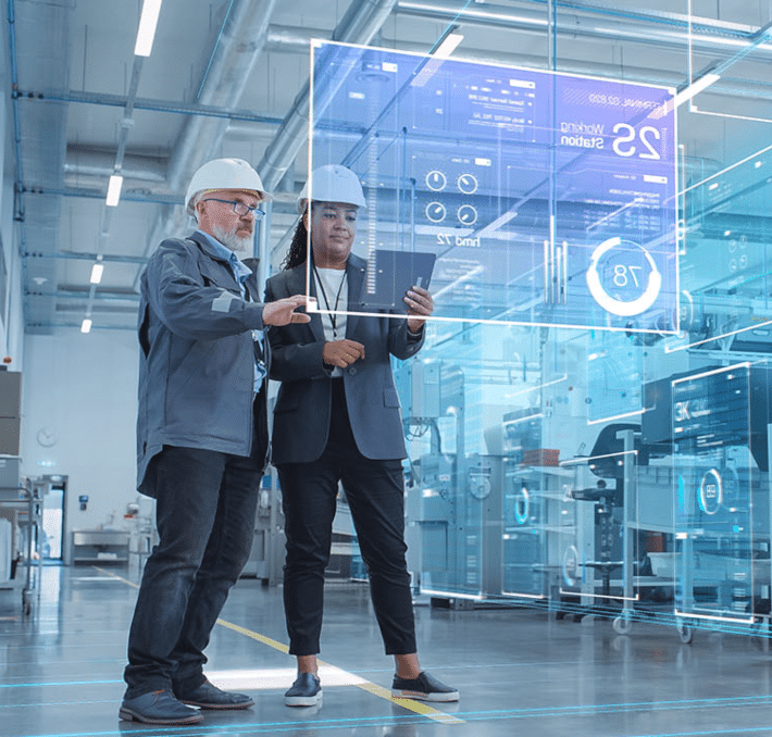 Two people in hard hats stand in a modern factory, interacting with a digital screen displaying data and analytics about industrial machinery, including CPQ for complex manufacturing solutions.