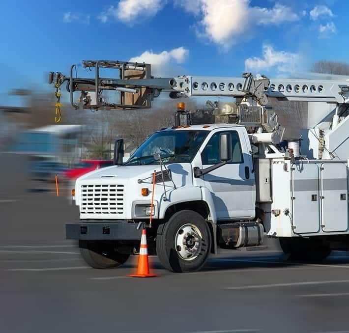 A white utility bucket truck is parked in a lot with two orange traffic cones placed near its front wheels.