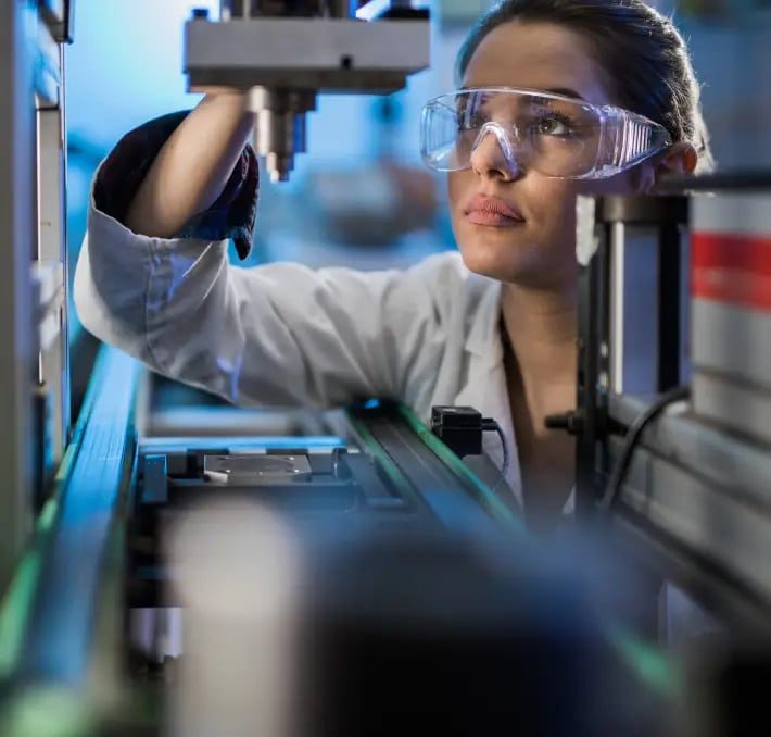 A person wearing safety goggles and a lab coat operates scientific equipment in a laboratory setting.
